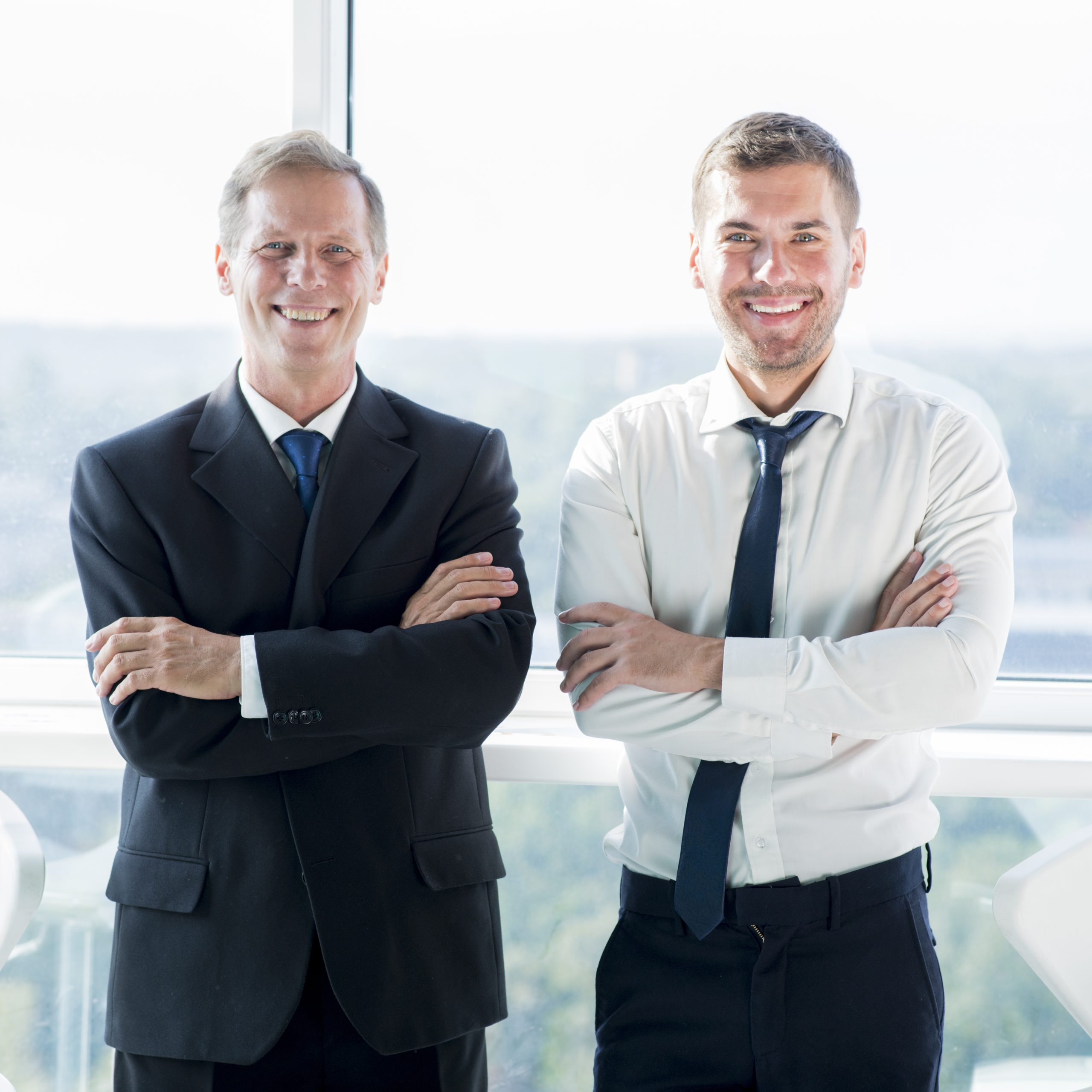 portrait-two-smiling-businessmen-standing-near-window